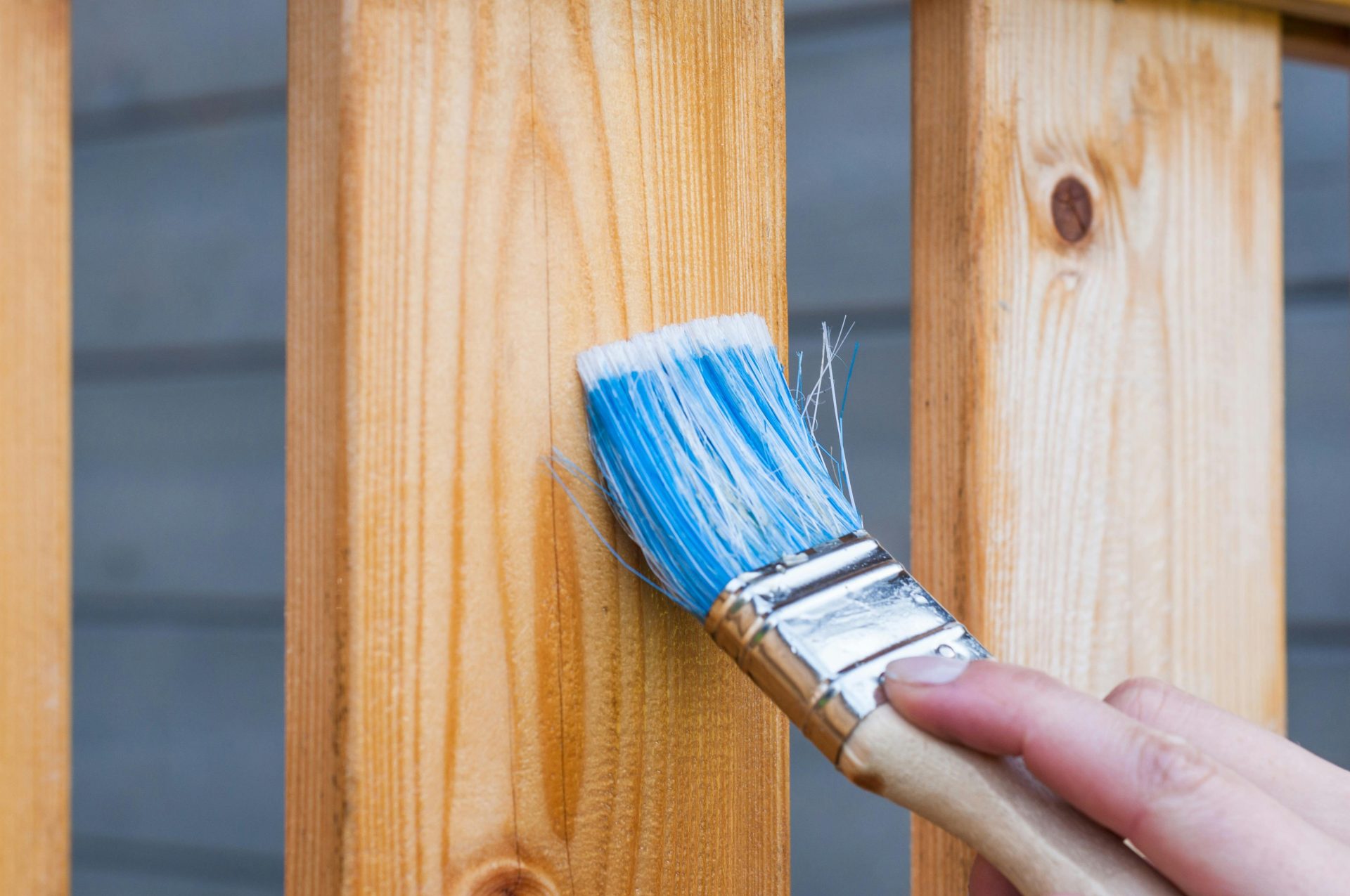 Una mano pintando una tabla de madera de una cerca con un pincel azul al aire libre. Ideal para proyectos de bricolaje y renovación.